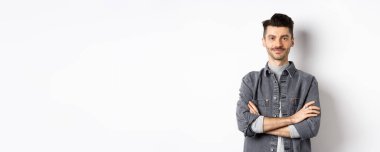 Kendine güveni tam yakışıklı bir adam göğsünde çapraz kollar, gülümsüyor, beyaz arka planda profesyonel duruyor..