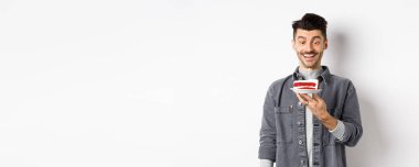 Doğum günü pastasında dilek tutan mutlu çocuk, gülümseyen ve yanan muma bakan heyecanlı, beyaz arka planda duran.