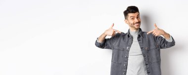 Yakışıklı adam, bıyıklı ve beyaz gülüşlü. Ortayı işaret ediyor, şirket logosunu gösteriyor, beyaz arka planda duruyor..