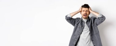 Hüsrana uğramış, ağlayan, panikleyen, ellerini başının üstüne koyup bağıran, sıkıntılı, beyaz arka planda üzgün duran bir adam..