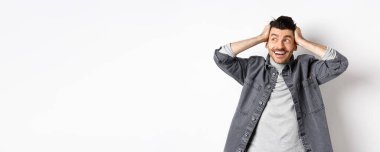 Heyecanlı genç adam rahatlamış ve mutlu görünüyor, gülümsüyor ve logoya bakıyor, el ele tutuşuyor neşeli, beyaz arka planda duruyor..