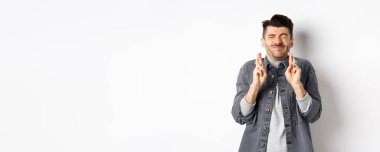 Umut dolu genç adam, gözleri kapalı ve parmakları kapalı, dilek diliyor, rüya için tanrıya yalvarıyor, haberleri bekliyor, beyaz arka planda duruyor..