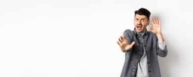 Korkmuş ürkek adam çığlık atıyor ve ellerini kaldırıyor. Durmak için yalvarıyor, saldırıdan korunuyor, beyaz arka planda duruyor..