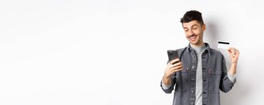 İnternetten alışveriş konsepti. İnternetten alışveriş yapan yakışıklı bir adam. Plastik kredi kartı gösteriyor. Akıllı telefona bakıyor..