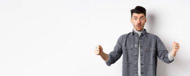 Kafası karışmış bir adam büyük bir nesne tutuyor ve şok olmuş görünüyor, büyük bir şeyi şekillendiriyor, beyaz arka planda duruyor..