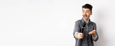 Yakışıklı gülümseyen adam mikrofonla elini uzatıyor, mikrofonu sana veriyor, beyaz arka planda duruyor..