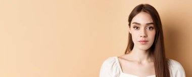 Doğal makyajlı, rahat yüzlü, bej arka planda duran güzel bir kadın yüzü..