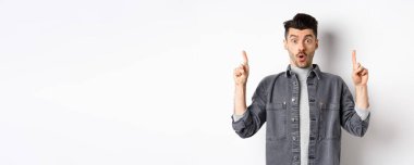 Heyecanlı adam reklam teklifini kontrol ediyor, şaşırıyor ve parmaklarını havaya kaldırıyor, havalı bir duyuru yapıyor, beyaz arka planda duruyor..