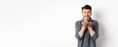 Tatlı genç adam kameraya hava öpücüğü yolluyor ve gülümsüyor. Umutsuz romantik aşkını gösteriyor, elinde bir şey tutuyor, beyaz arka planda duruyor..