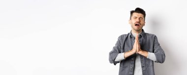 Sefil bir adam yardım için yalvarıyor, bir şeye ihtiyacı var ve ağlıyor, üzgün bir yüzle yalvarıyor, beyaz arka planda çaresizce duruyor..