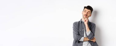 Düşünceli yakışıklı adam dalgın dalgın bakıyor, seçim yapıyor, beyaz arka planda duruyor..