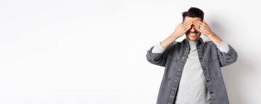 Mutlu, gülümseyen, gözleri kapalı bekleyen sürpriz bekleyen beyaz arka planda heyecanlı duran adam..