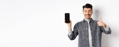 Neşeli stil sahibi adam boş akıllı telefon ekranı ve afişler gösteriyor, online alışveriş ve e-ticaret kavramı.