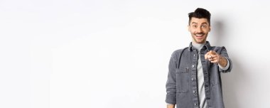 Bu sensin. Heyecanlı gülümseyen adam, neşeli yüzüyle kamerayı işaret ediyor. Beyaz arka planda kot ceketli adamı tanıyor..