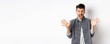 Kızgın adam çığlık atıyor ve kameraya bakıyor, öfkeli ve nefret dolu bir ifadeyle bağırıyor, beyaz arka planda duruyor..