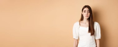 Lütfen. Onu istiyorum. Aptal kadın tatlı üzgün bakıyor ve ona bir şey almak için yalvarıyor, masum bir şekilde yalvarıyor, bej rengi arka plan..