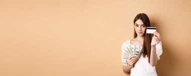 Plastik kredi kartı gösteren genç bir kadın, dolar yerine temassız ödemeyi tercih ediyor, bej arka planda duruyor..