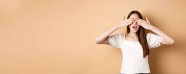 Mutlu romantik kız gözlerini kapatıyor ve sürpriz bekliyor, hediyeyi beklerken gülümsüyor, bej arka planda duruyor..