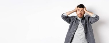 Paniğe kapılmış bir adam, paniğe kapılmış ve paniğe kapılmış bir şekilde logoya bakıyor, sorun yaşıyor, el ele tutuşuyor, beyaz arka planda duruyor..