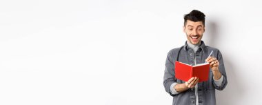 Ajandasında yazan, gülümseyen, günlük ya da günlüğe fikirler yazan, beyaz arka planda duran heyecanlı adam..