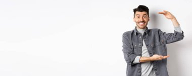 Neşeli adam gülümsüyor ve büyük boy gösteriyor, büyük bir şey gösteriyor ve heyecanlı görünüyor, beyaz arka planda duruyor..