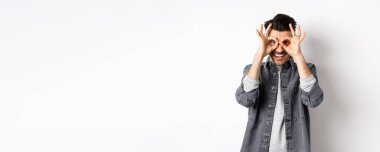 Gülümseyen komik adam, el dürbününden güzel bir teklif görüyor, mutlu ve heyecanlı görünüyor, reklamlara bakıyor, beyaz arka planda duruyor..