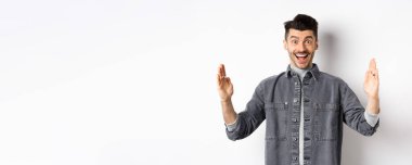 Bıyıklı mutlu bir adam gururlu bir gülümseme ile büyük bir nesne şekillendiriyor, beyaz arka planda ceketle duruyor..