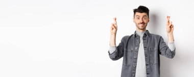 Umut gerçek olur. Pozitif ve yakışıklı adam umut dolu görünüyor ve kameraya gülümsüyor, sonuçları bekliyor, beyaz arka planda duruyor..