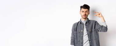 Hayal kırıklığına uğramış, küçük boylarda, suratını buruşturan üzgün, küçük şeylerden rahatsız olan, beyaz arka planda duran biri..