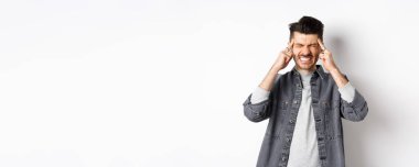 Baş ağrısı çeken, baş ağrısından dişlerini sıkan, baş şakaklarına dokunan, migren ağrısı çeken, beyaz arka planda duran, ağrı kesicilere ihtiyacı olan bir adam..