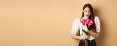 Sevgililer Günü. Şaşırmış kız sevgilisinden hediye alıyor, güzel bir buket çiçeğe bakıyor, elinde bej arka planda güller tutuyor..