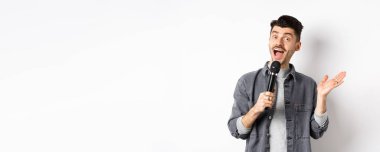 Heyecanlı stil sahibi adam konuşma yapıyor, mikrofonla konuşuyor, karaoke yapıyor ya da şarkı söylüyor, beyaz arka planda duruyor..