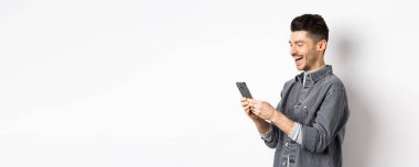 Telefonda sohbet eden, gülen ve akıllı telefon ekranı okuyan, beyaz arka planda duran yakışıklı adamın profili..