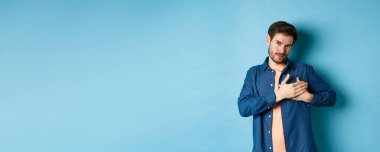 Romantik bir adam kalbi kucaklıyor ve gülümsüyor, teşekkür ediyor, mavi arka planda minnettar duruyor..