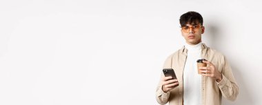 Gerçek insanlar. Süslü hippi adam elinde kahve bardakları ve cep telefonuyla beyaz arka planda duruyor..