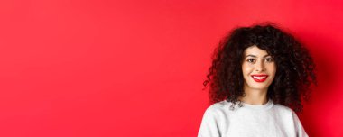 Kırmızı dudaklı, kıvırcık saçlı, gülümseyen ve mutlu görünen güzel bir bayan..