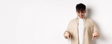 Gözlüklü şık modern adam, mutlu bir gülümsemeyle aşağı bakıyor, afişi gösteriyor, beyaz arka planda duruyor..