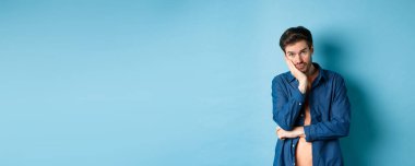 Üzgün ve sıkılmış bir adam elinde eğilmiş kameraya boş kafayla bakıyor, mavi arka planda sıkıntılı duruyor..