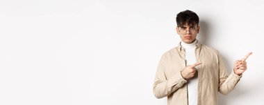 Kızgın genç adam somurtuyor ve sağ üst köşe afişini işaret ediyor, şikayet ediyor ve hayal kırıklığına uğramış görünüyor, beyaz arka planda duruyor..