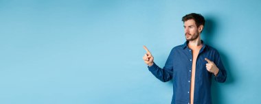Kafkasyalı genç bir adamın görüntüsü, bir kenara bakıyor, reklamını yapıyor, mavi arka planda duruyor..