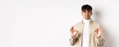 Fena değildi. Tatmin olmuş genç bir adam güzel jestler yapıyor ve onaylayarak başını sallıyor, iyi iş çıkarıyor, sonuçlardan memnun, beyaz arka planda duruyor..