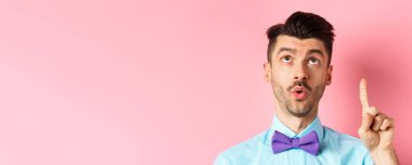 İlgi çekici bıyıklı genç adam, işaret ediyor ve ilginç bir şeye bakıyor, reklamlara bakıyor, pembe arka planda duruyor..