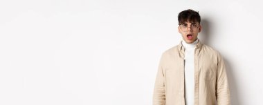 Şok olmuş gözlüklü genç adamın portresi. Çenesini indir, ağzını aç ve kameraya bak. Etkileyici bir şeye bak..