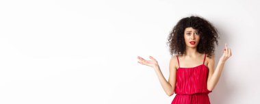 Annoyed caucasian woman in red dress, showing finger without wedding ring, arguing about marriage, standing pissed-off on white background.