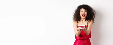 Tatiller ve kutlama konsepti. Kırmızı elbiseli, gülümseyen kadın sana mumlu doğum günü pastası veriyor, beyaz arka planda duruyor..