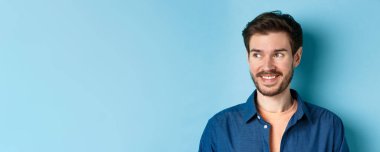 Sakallı, boş alana bakıp gülümseyen, mavi arka planda duran yakışıklı, kendine güvenen bir adama yaklaş..