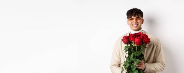 Yakışıklı hippi bir buket gülle sevgilisini bekliyor. Sevgililer gününde beyaz arka planda duran çiçekli genç adam..