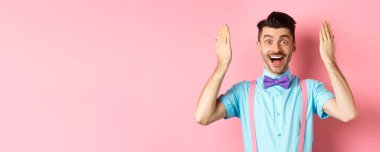 Neşeli genç adam sürpriz bir hediye için gözleri açık, hediyeye hayran bakıyor, pembe arka planda duruyor..