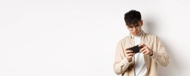 Cep telefonuyla video oyunu oynayan yakışıklı bir gencin portresi, akıllı telefonu yarış için eğmek, beyaz arka planda durmak..