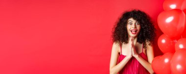 Sevgililer Günü. Heyecanlı, beyaz elbiseli bir kadın şaşkınlıktan atlıyor, alaycı bir şeye bakıyor, ürün almak istiyor, kalp balonlarının yanında duruyor, beyaz arka plan.